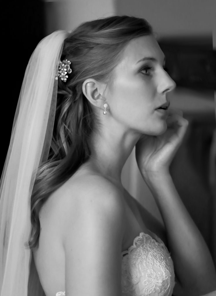 Braut mit Schleier legt ihren Ohrring an