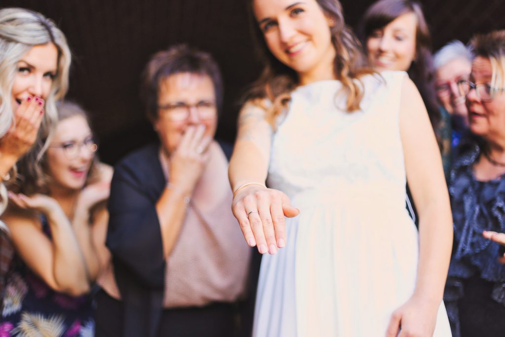 Braut zeigt ihren Ehering, während Freundinnen im Hintergrund staunen