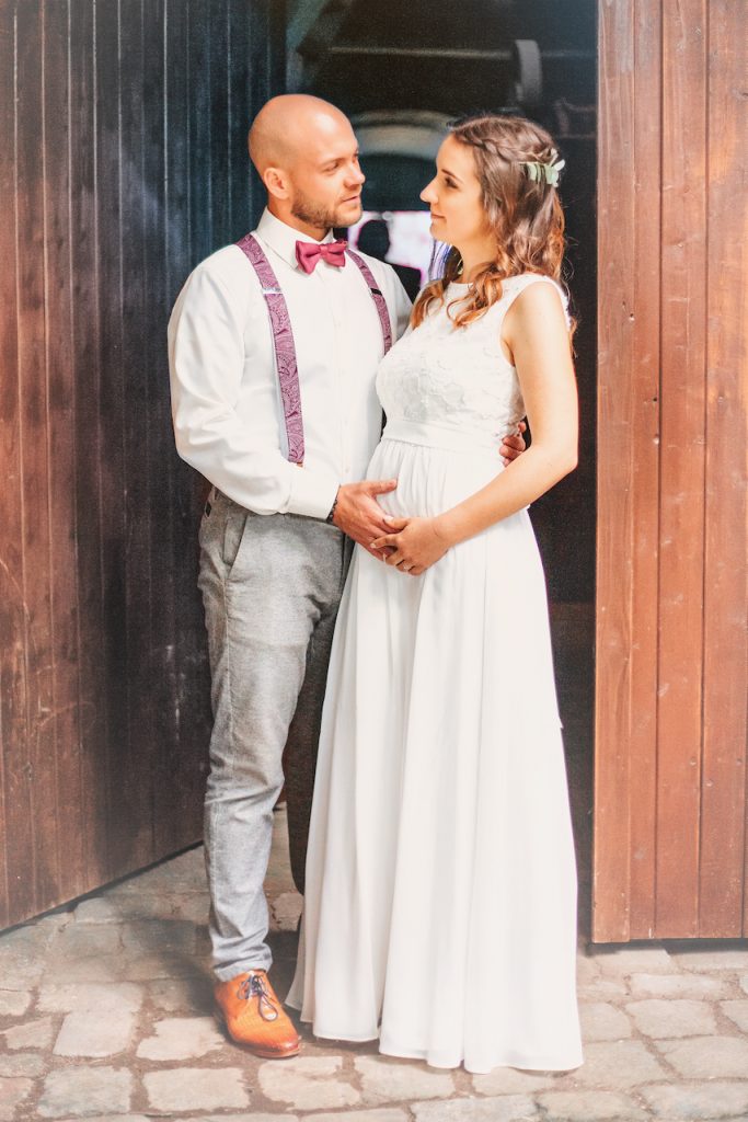 Brautpaar schaut sich verliebt an und legt die Hände auf Babybauch