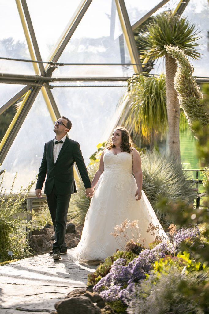 Brautpaar geht Hand in Hand durch einen botanischen Garten