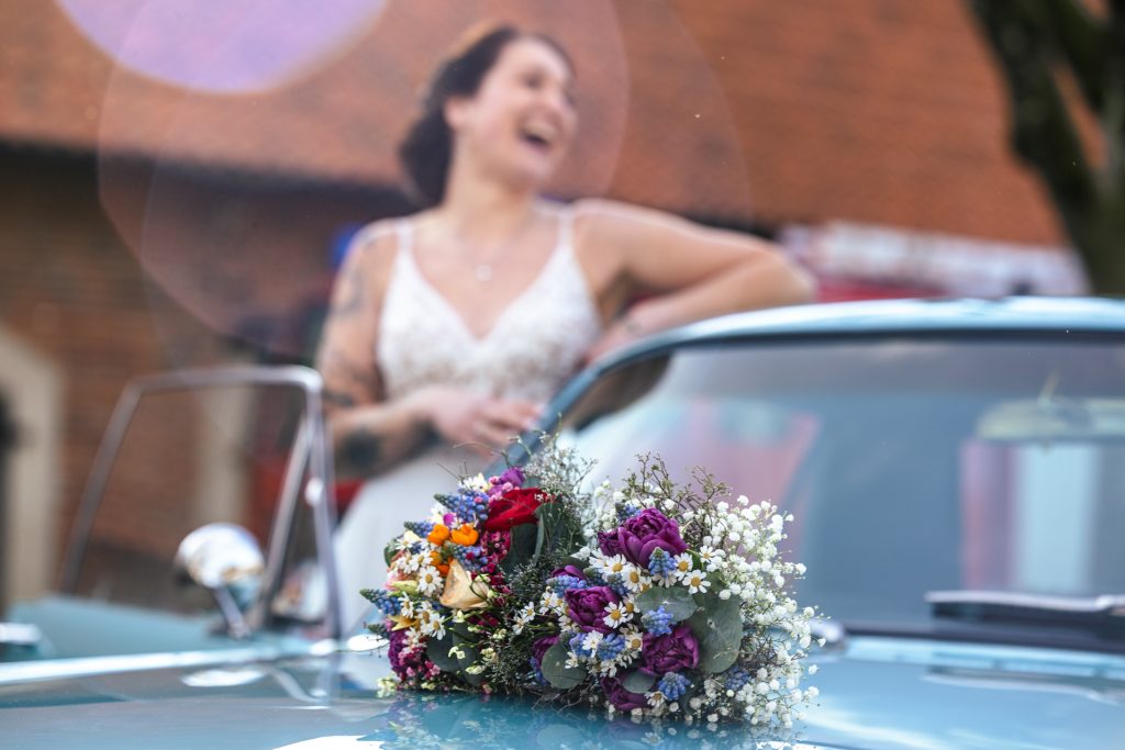 Foto mit einem Brautstrauß im Vordergrund und einer lachenden Braut im Hintergrund